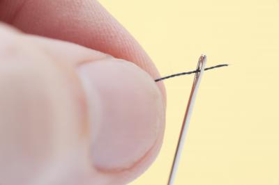 Person threading a needle with yarn